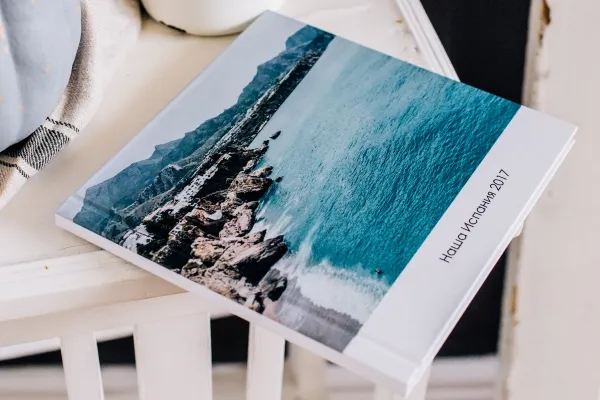 Квадратная фотокнига в твердом переплете. На обложке море и подпись Наша Испания 2017