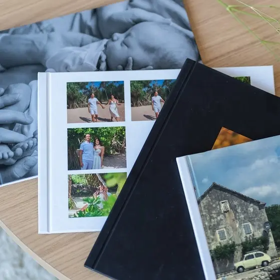 На столе лежат несколько фотокниг. На фотографиях парень и девушка на отдыхе, новорожденный младенец на руках